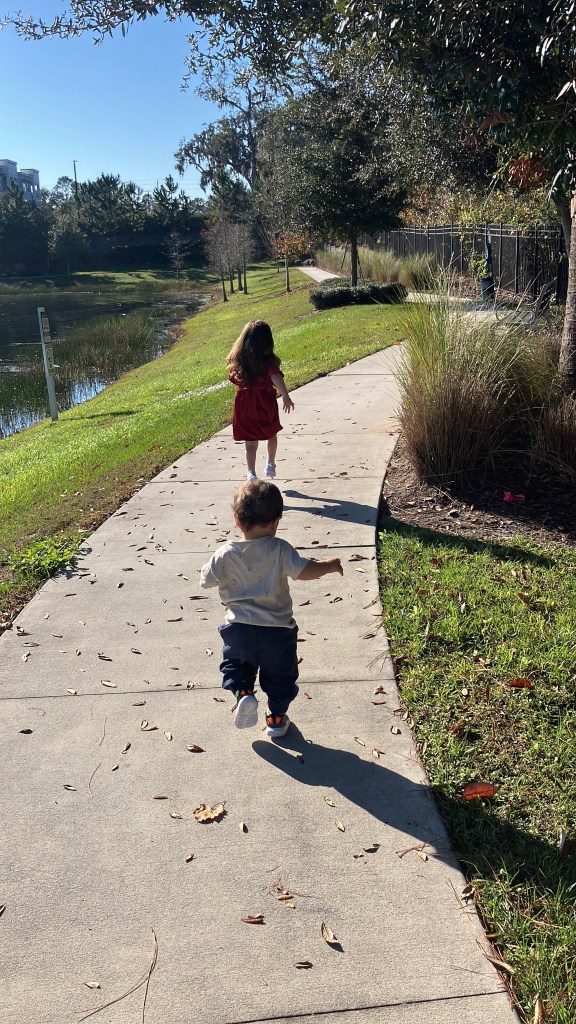 author's two kids running on a sidewalk by a pond
